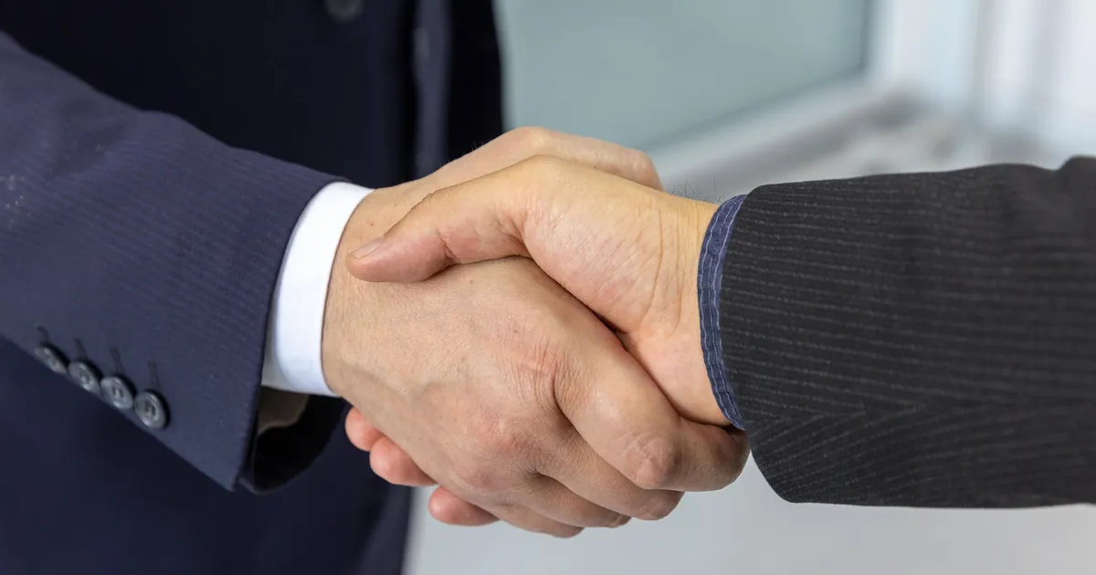 Two people in business suits shaking hands to close a deal